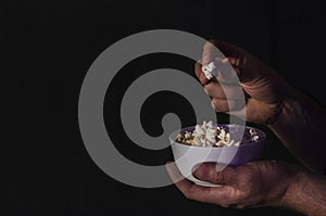 Popcorn in a cup in the hands of a man watching a movie on a black background with copy space. For articles about the movie