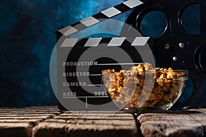 Popcorn film reel and movie clapper on wood background. Screensaver for the inscription of the rest of the viewing of films.