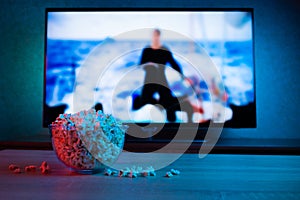 Popcorn in a glass plate on the background of the TV. Color bright lighting, blue and red. Background