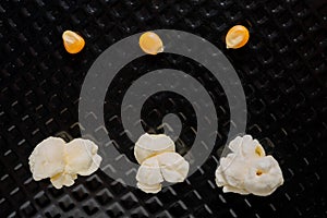 Popcorn grains popped and not popped in top view, and closeup and black textured background
