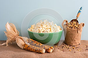 Popcorn in a Green Vintage bowl with multicolored, dried corn cobs and unpopped kernels in a container all on burlap table with bl