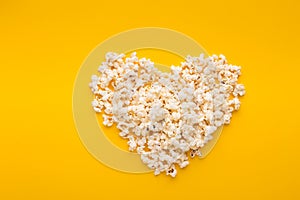 Popcorn in heart shape on yellow background, top view