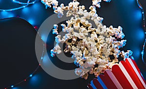 Popcorn, movies and entertainment concept on black background with blue neon light, flatlay