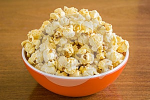 Popcorn in orange bowl. Brown background