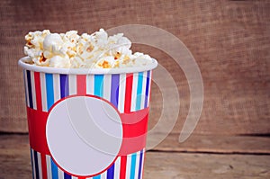Popcorn in paper cup on wooden surface. Copy space