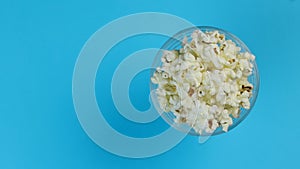 Popcorn in a plate on one edge of the frame, rotating on a blue background. Space for text.