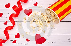 Popcorn, red hearts and ribbon on a white wooden background. valentine`s day, movie theater