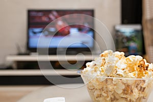 Popcorn and remote control on sofa with a TV broadcasting wrestling