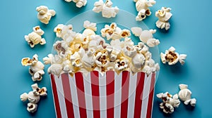 Popcorn scattered from red striped box on pastel blue background with space for text placement