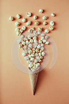 Popcorn spills out of waffle cone on beige background, snack, concept flat lay photography and content for food blog
