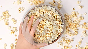 Popcorn tossed in a wooden bowl on a white background. Slow Motion video. female hand takes popcorn. Close up top view