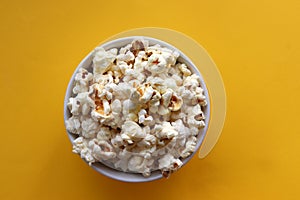 Popcorn in a white bowl on yellow colored background. Top view, copy space