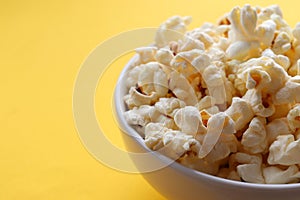 Popcorn in a white bowl on yellow colored background. Top view, copy space