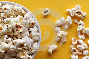 Popcorn in a white bowl on yellow colored background. Top view, copy space