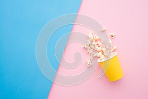 Popcorn in yellow paper party cup on colorful blue pink background.