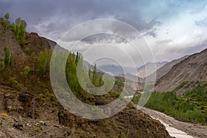 Poplar trees and small running river small lying in a rocky valley underlying blue cloudy sky