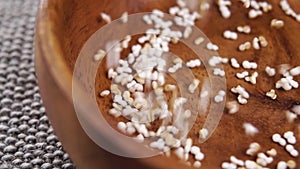 Popped dry amaranth falls into a rustic wooden bowl in slow motion on a jute cloth