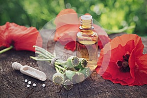 Poppies, poppy flower heads, bottle of infusion and scoop of homeopathic globules.