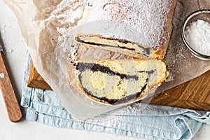 Poppy seed roll or strudel on wooden board sprinkled with powdered sugar.