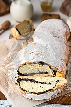 Poppy seed roll or strudel on wooden board sprinkled with powdered sugar.