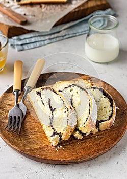 Poppy seed roll or strudel on wooden board sprinkled with powdered sugar.