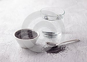 Poppy seeds in bowl and glass of water for poppy milk on light gray background