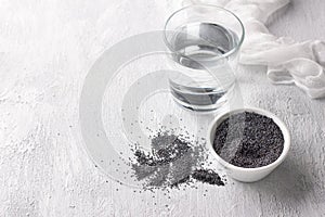 Poppy seeds in bowl and glass of water for poppy milk on light gray background