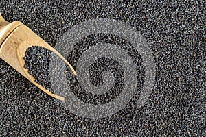 Poppy seeds. Dark pile poppyseed food in wooden scoop or spoon isolated on black stone background. Vitamin snack breakfast, diet