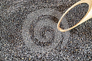 Poppy seeds. Dark pile poppyseed food in wooden scoop or spoon isolated on black stone background. Vitamin snack breakfast, diet