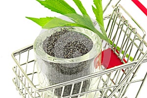 Poppy seeds with green leaves in bowl in shopping trolley on white background