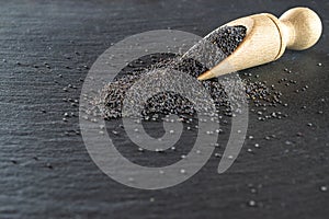 Poppy seeds isolated on dark stone background in wooden scoop. Pile poppyseed food in spoon on black. Healthy breakfast