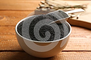 Poppy seeds and scoop in bowl on wooden table