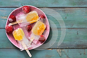 Popsicle with orange slices on a pink plate, frozen strawberries. Green rustic background. Top view, place for text. Summer desser