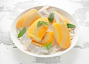 Popsicles, ice lollies on stick with sweet orange juice in white plate with ice