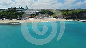 Popular beach for holidays in Bali with surfers in blue ocean. Aerial view of Dreamland beach