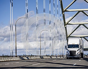 Popular big rig white long hauler semi truck transporting cargo in dry van semi trailer driving on the road on the truss arched