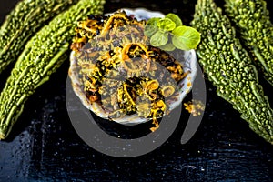 Popular dish for serving in lunch i.e. Bitter gourd with spices and vegetables on wooden surface in a glass plate with raw karela,