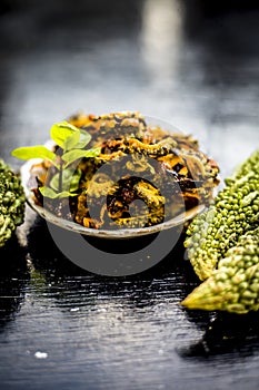 Popular dish for serving in lunch i.e. Bitter gourd with spices and vegetables on wooden surface in a glass plate with raw karela,