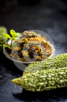 Popular dish for serving in lunch i.e. Bitter gourd with spices and vegetables on wooden surface in a glass plate with raw karela,