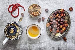 Popular food during Iftar - macadamia nuts, pistachios, walnuts, dry dates. Karan, rosary, teapot, bowl with black tea on concrete