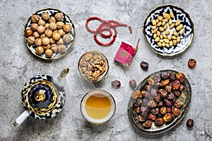 Popular food during Iftar - macadamia nuts, pistachios, walnuts, dry dates. Karan, rosary, teapot, bowl with black tea on concrete