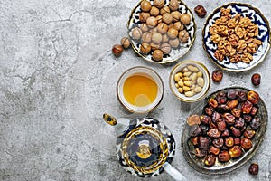 Popular food during Iftar - macadamia nuts, pistachios, walnuts, dry dates. Karan, rosary, teapot, bowl with black tea on concrete