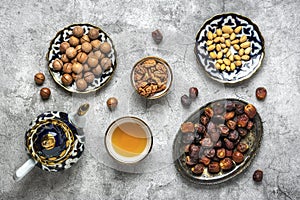 Popular food during Iftar - macadamia nuts, pistachios, walnuts, dry dates. Karan, rosary, teapot, bowl with black tea on concrete