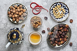 Popular food during Iftar - macadamia nuts, pistachios, walnuts, dry dates. Karan, rosary, teapot, bowl with black tea on concrete