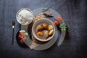 Popular Indian lunch ingredient egg curry in a bowl along with rice and salad condiments.