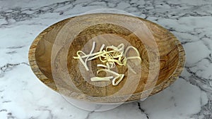 Popular pasta usually used for broth falling into wooden bowl. Marble worktop background