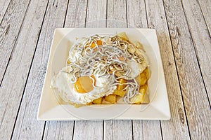 Popular Spanish shared dish of broken eggs with diced fried potatoes and eels on light colored table