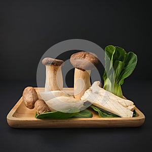 Popular uncooked healthy asian edible King Oyster mushrooms and Baby Bok Choy on wooden plate on black background.