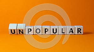 Popular or unpopular symbol. Turned wooden cubes and changed the word unpopular to popular. Beautiful orange table, orange photo