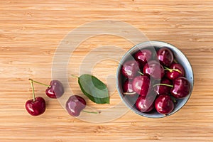 Porcelain bowl with ripe dark red stella cherries on bamboo chopping board with copy space